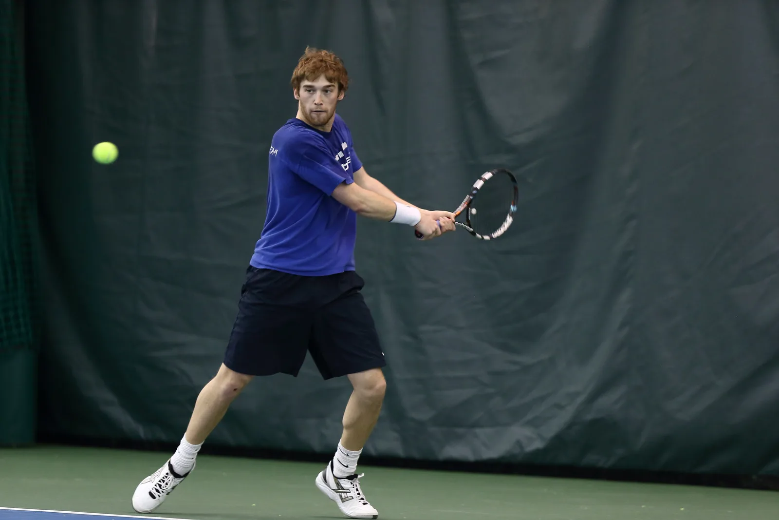 Sam Sweeney hitting a backhand on an indoor court