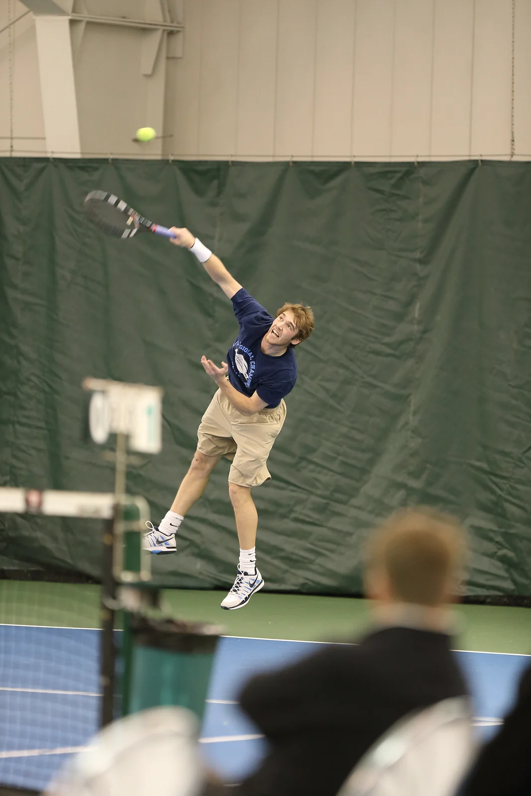 Sam Sweeney airborne on a serve at an indoor regional match
